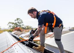 A professional electrician near me from ABA Electrical working safely on a rooftop with harness and tools, delivering expert electrical installation services.